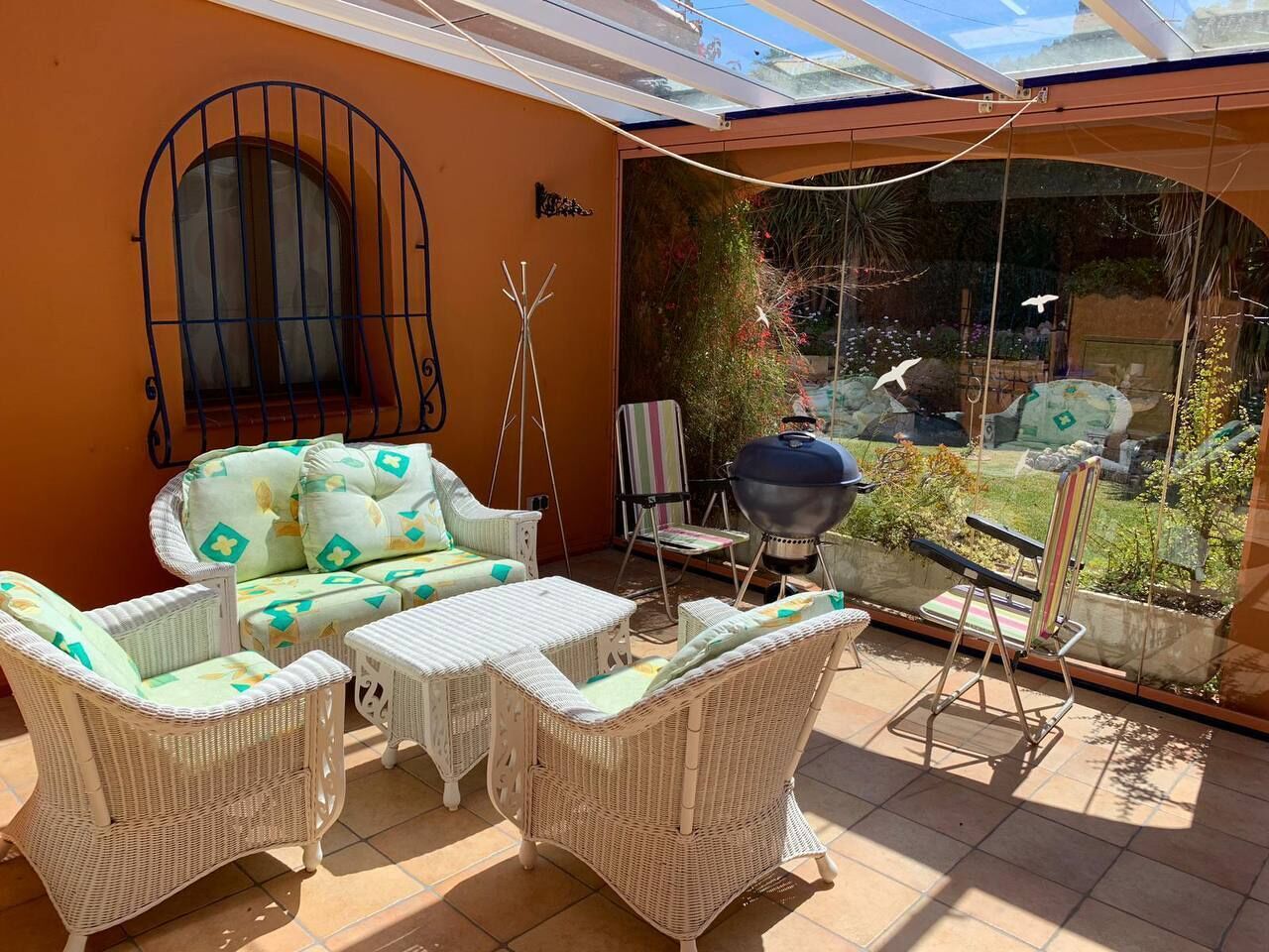 A patio area with wicker furniture, a grill, and a view of a garden.
