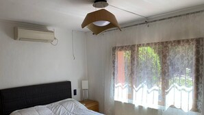 A bedroom with a bed, a nightstand, a lamp, an air conditioner, and a window with curtains. - Casa Javea (Jávea)
