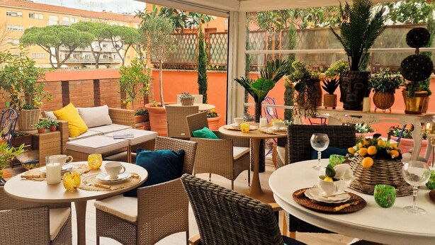 A sunlit patio area with wicker furniture, round tables, and potted plants. - Vaticano 13 guesthouse (Rome)