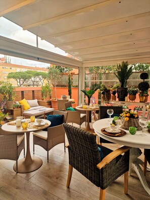 En solbeskinnet terrasse med fletningsmøbler, runde borde og krukker med planter.