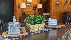A wooden cabin interior with a dining table set with jars, a plant, and a decorative item. - Lakefront Lincoln Log home at Locke Lake Colony Association (Barnstead)