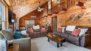 A cozy log cabin interior with a living room featuring a brown leather sofa set, a wooden coffee table, and a ceiling fan. - Lakefront Lincoln Log home at Locke Lake Colony Association (Barnstead)
