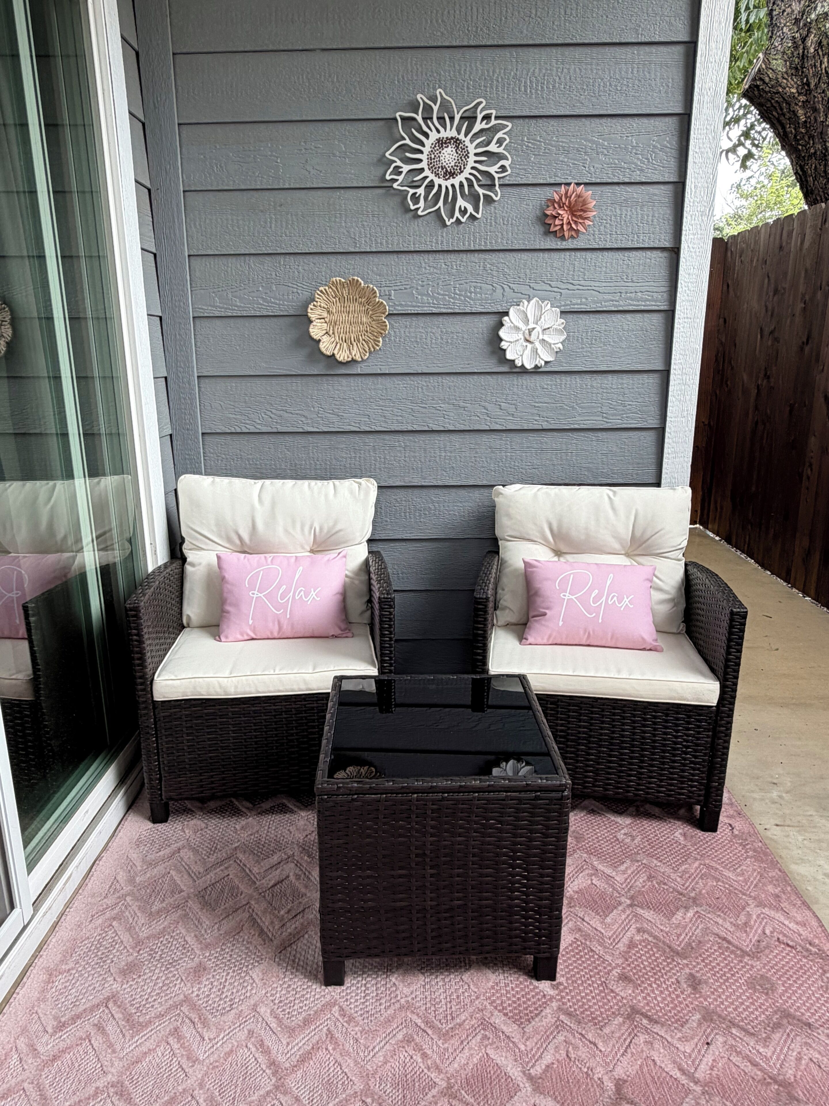 A wicker sofa with cushions, a small table, and decorative wall art against a grey wall.