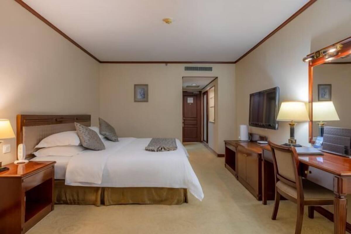 Une chambre d’hôtel comprenant un lit, une table de chevet, une lampe, un bureau, une chaise, une télévision et un miroir.
