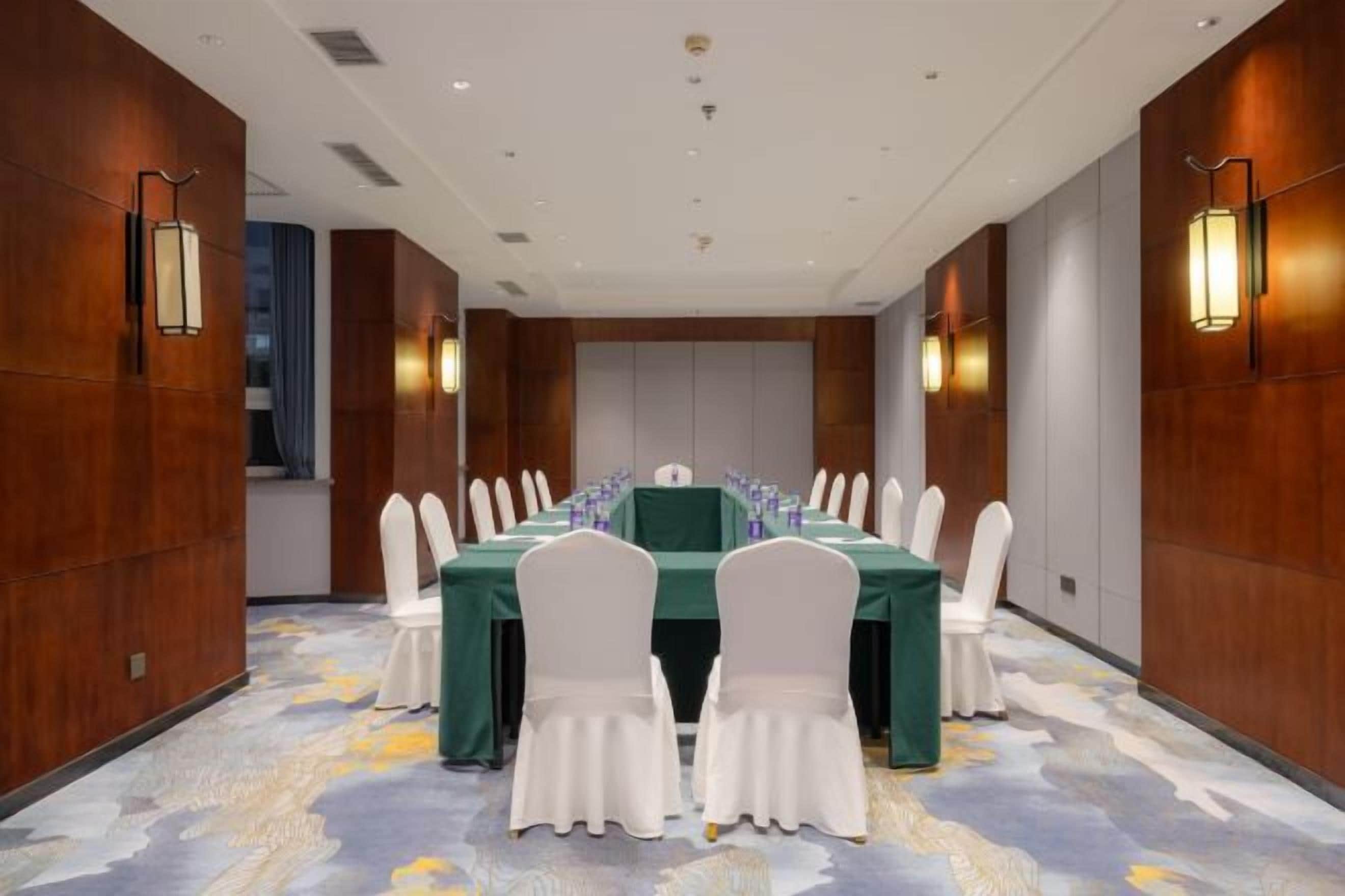 Un salón de conferencias con una larga mesa, sillas blancas y un mantel verde.
