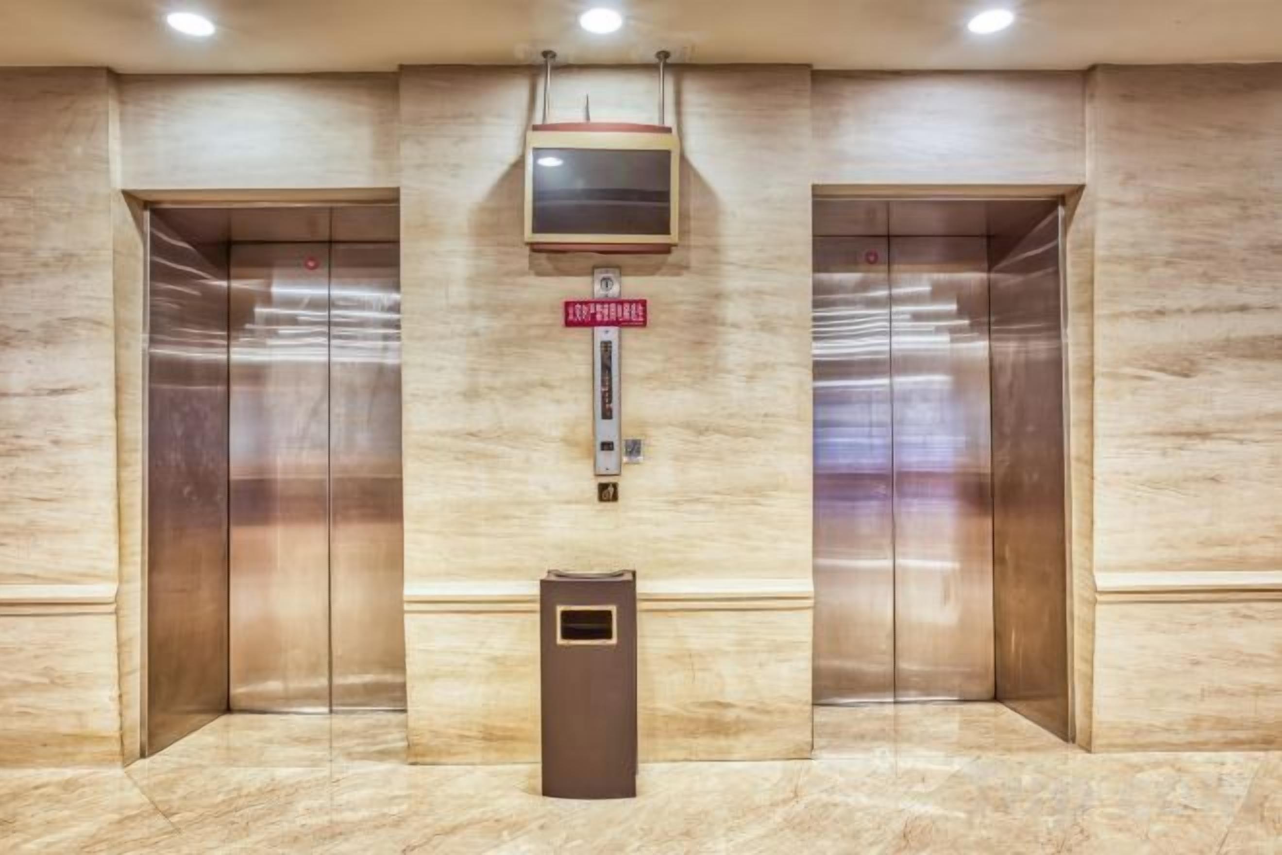 Een lift met een digitaal display, een brandmelder en een prullenbak.