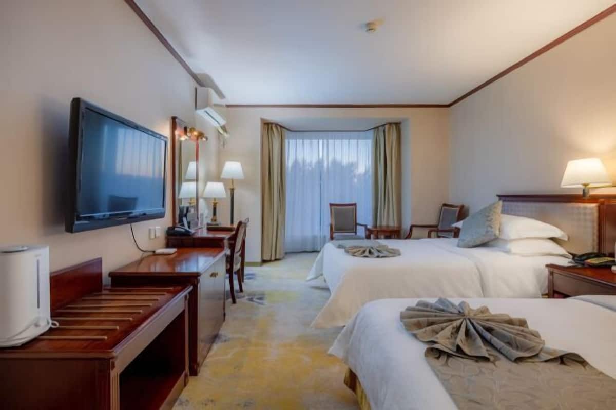Une chambre d’hôtel avec deux lits, un bureau, une télévision et une grande fenêtre avec des rideaux.