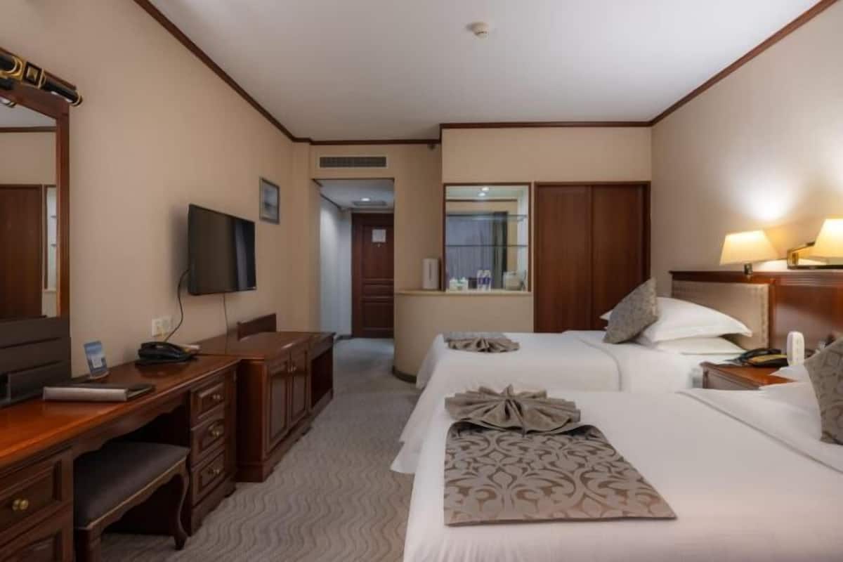 Une chambre d’hôtel équipée d’un bureau, de deux lits, d’une télévision et d’une salle de bain que l’on aperçoit à l’arrière-plan.