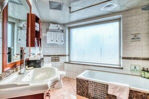 A modern bathroom with a large bathtub, a separate toilet, a vanity with a mirror, and a window providing natural light. - Changchun Celebrity Hotel (Changchun)