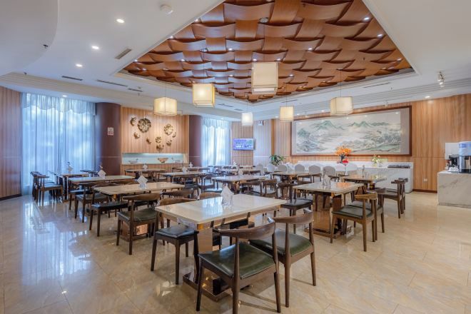 Un vaste espace de restauration dans l’hôtel, avec de nombreuses tables et chaises, un plafond en bois décoratif et un grand tableau accroché au mur.