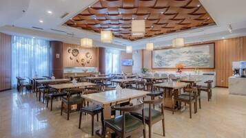 Un vaste espace de restauration dans l’hôtel, avec de nombreuses tables et chaises, un plafond en bois décoratif et un grand tableau accroché au mur.
