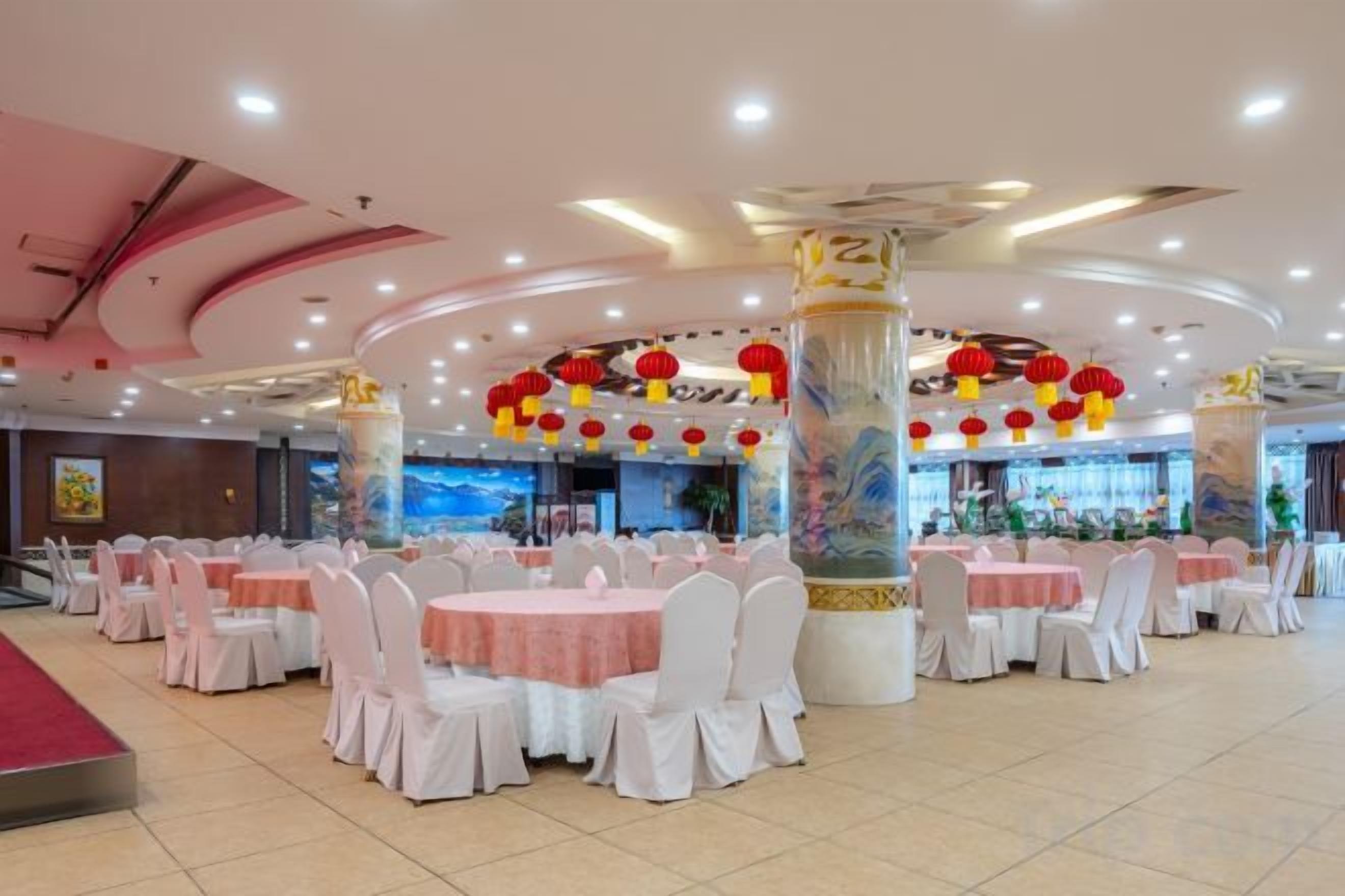 Une salle de banquet avec des tables rondes, des chaises blanches et des lanternes rouges.