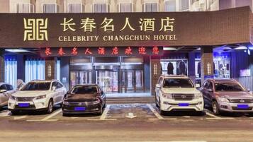 Entrada de un hotel con un letrero que dice 'Celebrity Changchun Hotel' y varios coches estacionados frente a él.