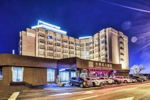 A multi-story hotel with a prominent sign, a parking area with several cars, and a clear night sky. - Changchun Celebrity Hotel (Changchun)