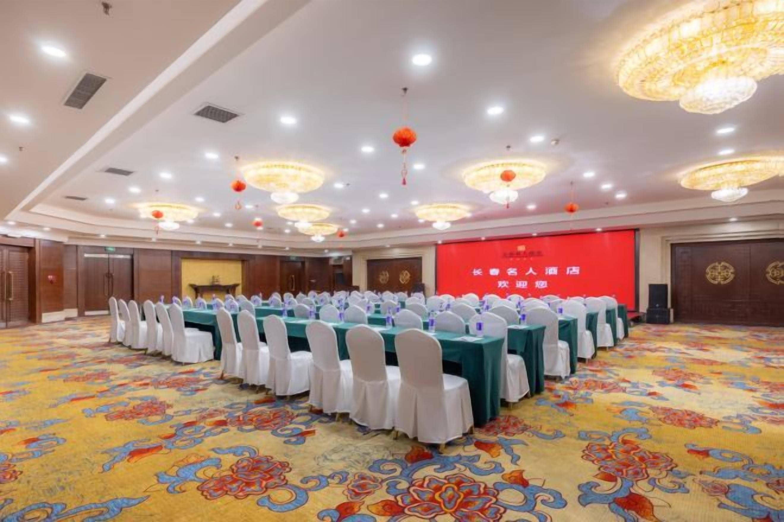 Un salón de conferencias con mesas redondas, sillas blancas y piso alfombrado.