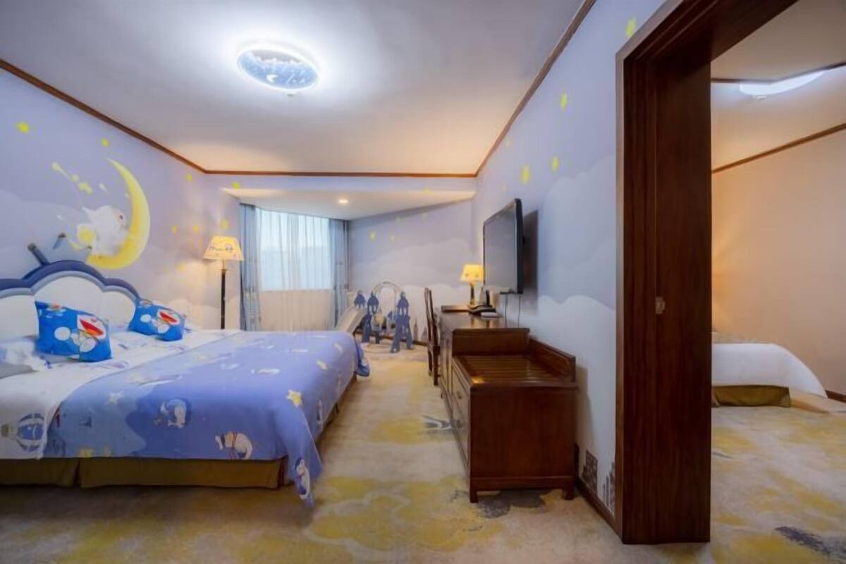 Une chambre d’hôtel avec deux lits, une commode en bois, une télévision et une fresque représentant la lune et les étoiles sur le mur.