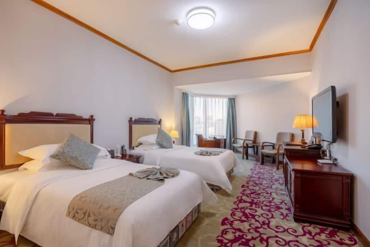 Une chambre d’hôtel avec deux lits, un bureau, une chaise, une télévision et une fenêtre avec des rideaux.