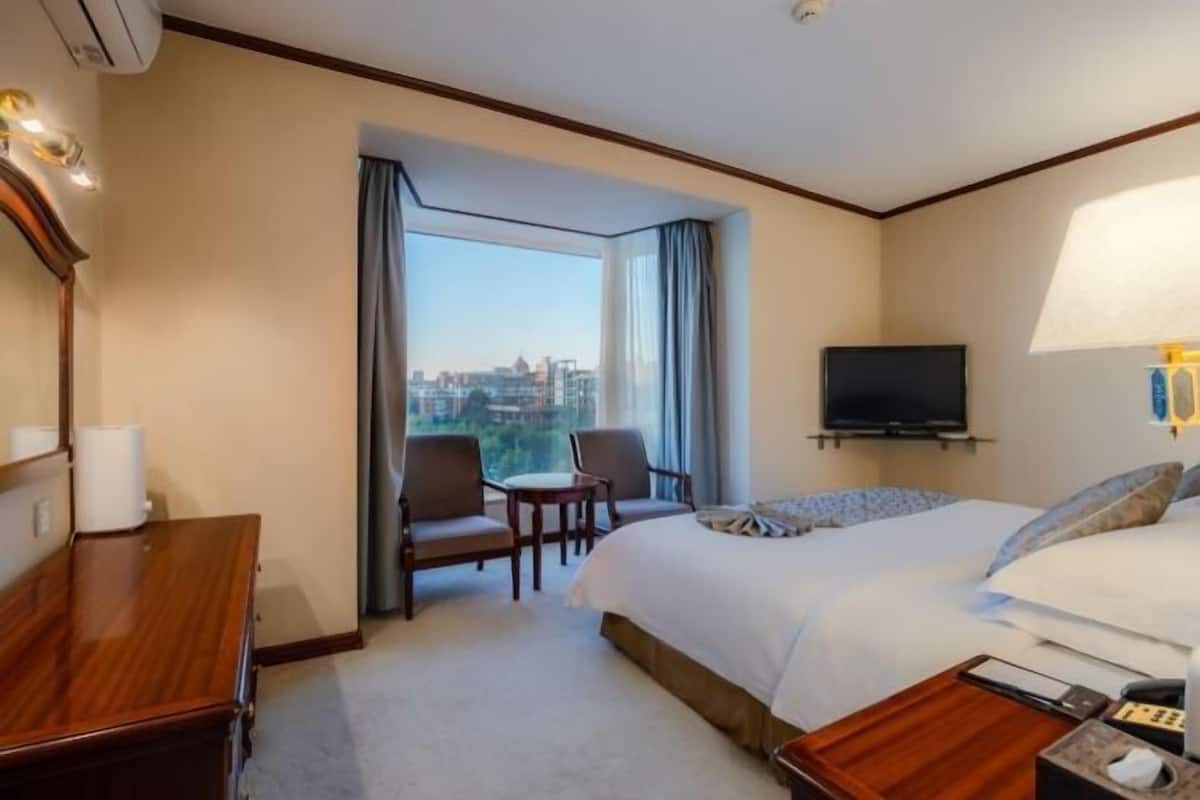Une chambre d’hôtel avec un grand lit, un bureau, une chaise, une télévision et une fenêtre donnant sur la ville.