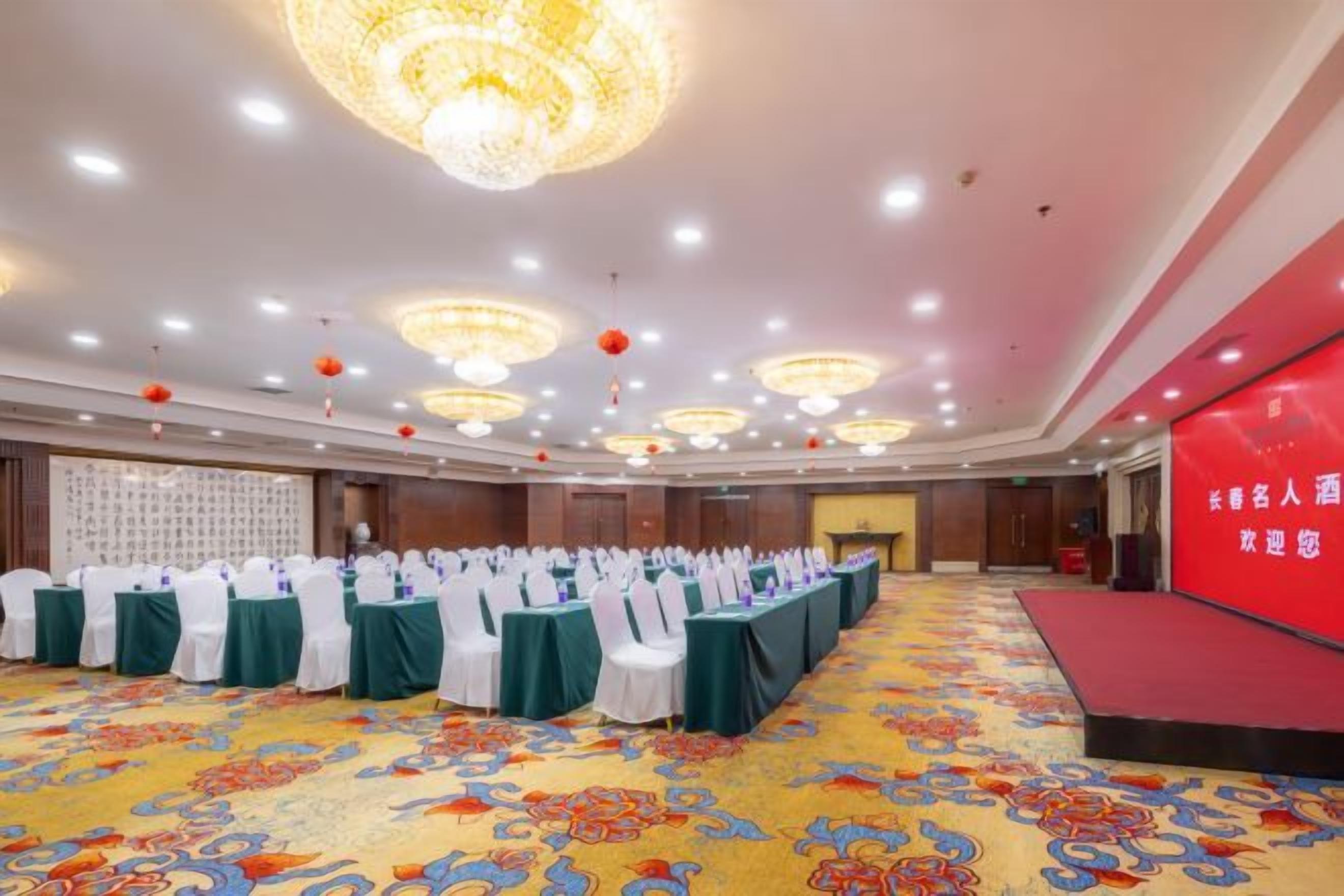 A banquet hall with rows of tables, a stage, and a red wall with text.