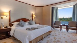 A hotel room with a large bed, two bedside lamps, a nightstand, a chair, a small table, and a view of the outdoors. - Changchun Celebrity Hotel (Changchun)