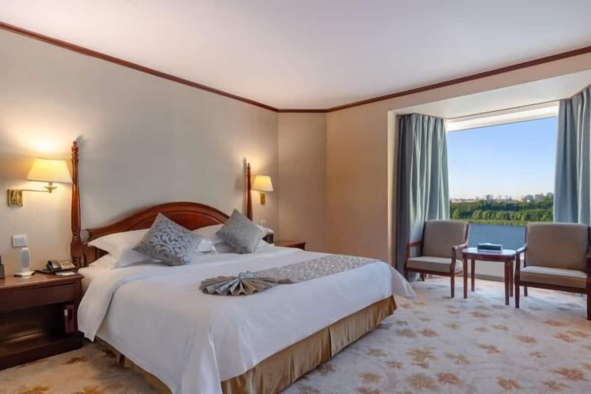 Une chambre d’hôtel avec un grand lit, deux lampes de chevet, une table de chevet, une chaise, une petite table et une vue sur l’extérieur.