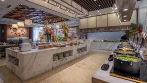 Un hall d’hôtel moderne avec un comptoir d’accueil en marbre, un espace buffet proposant divers plats et des compositions florales décoratives.