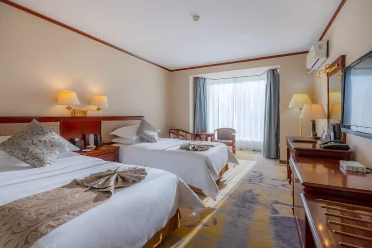 Une chambre d’hôtel avec deux lits, un bureau, une chaise et une grande fenêtre avec des rideaux.