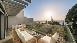 A balcony with wicker furniture, a glass railing, and a view of the ocean at sunset. - With pool, in Funchal - Acqua Residence II (Funchal)