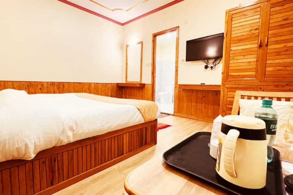 A hotel room with a wooden bed, a black tray with a mug and a bottle, and a television on the wall.