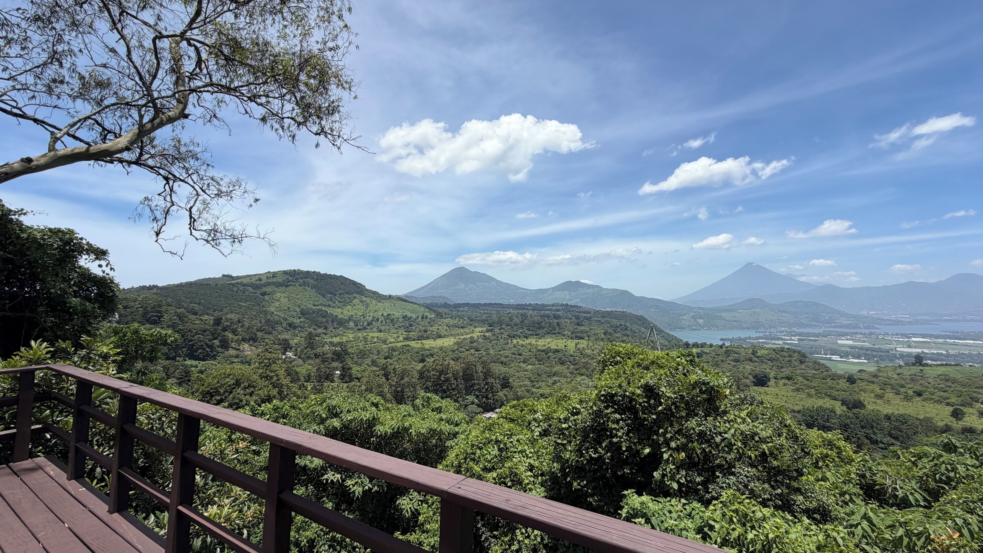 A scenic view from a wooden deck overlooking a lush landscape with hills and a distant mountain.