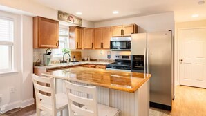 A kitchen with wooden cabinets, a stainless steel refrigerator, a microwave, and a sink.