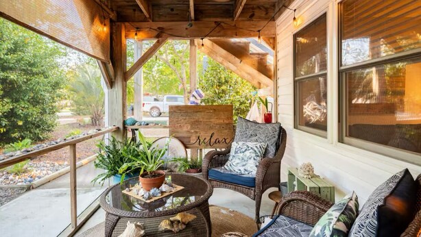 A cozy porch with wicker furniture, a glass table, and potted plants.
