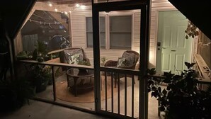 A covered patio with a seating area, a door leading to a room, and string lights.