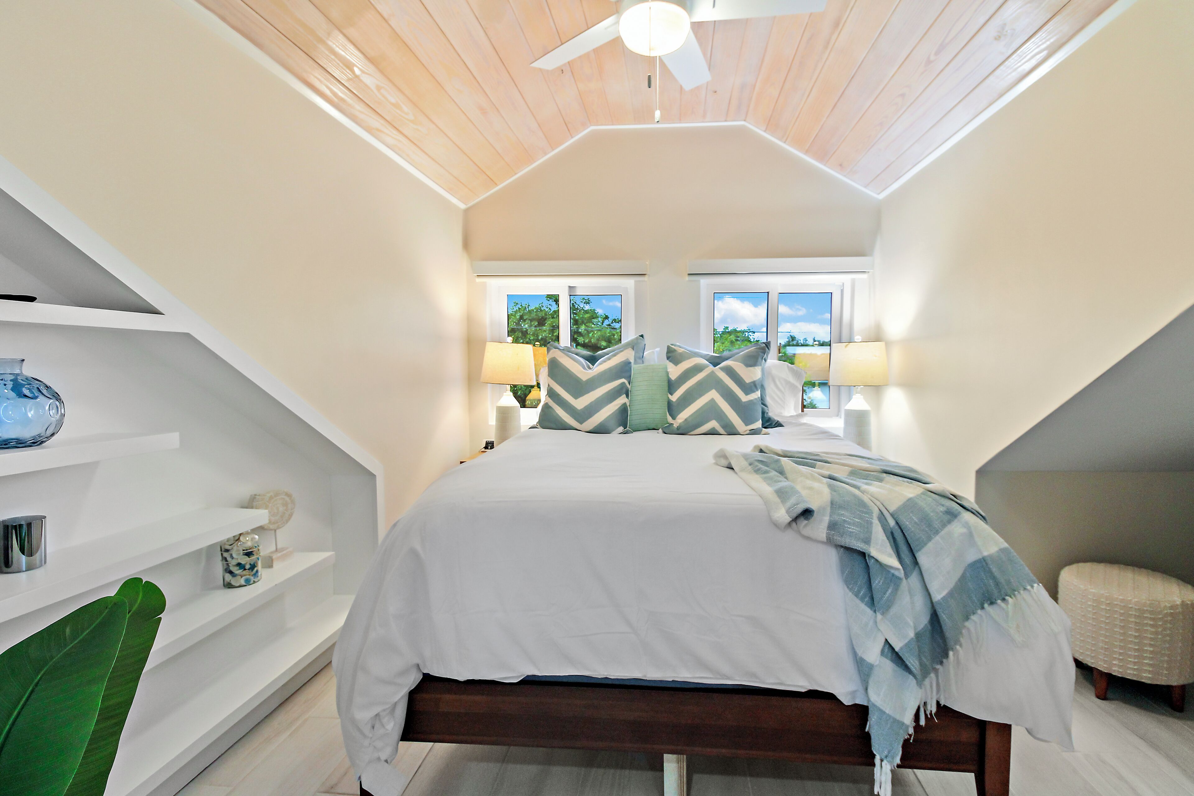A bedroom with a bed, two windows, a ceiling fan, and a nightstand with a lamp.
