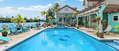 A swimming pool with lounge chairs and potted plants, surrounded by a house with a view of the water.