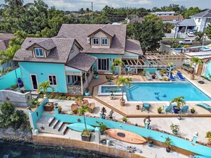 Ein großes Haus mit Swimmingpool, Sitzgelegenheiten im Freien und einem Boot, das im Hafen liegt.