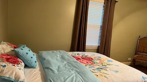A bedroom with a bed, floral bedspread, and a window with curtains. - Pink Door Charming 2-bedroom house with WiFi, AC in nice Oneonta, Close to Food (Oneonta)