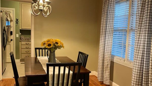 A dining area with a wooden table and chairs, a chandelier, and a vase with sunflowers. - Pink Door Charming 2-bedroom house with WiFi, AC in nice Oneonta, Close to Food (Oneonta)