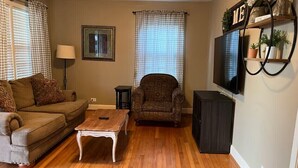 A living room with a sofa, armchair, coffee table, TV, and a shelf with plants. - Pink Door Charming 2-bedroom house with WiFi, AC in nice Oneonta, Close to Food (Oneonta)
