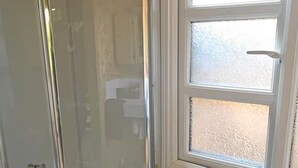A glass-enclosed shower with a metal towel rack holding two towels, a window above, and a wooden wall. - Parry’s hideaway, cosy little cabin by the stream, listening to the birds. (Exmouth)