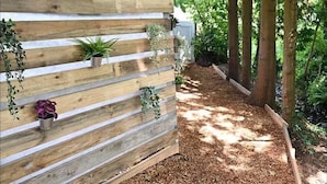 A wooden wall with plants and a pathway covered in mulch. - Parry’s hideaway, cosy little cabin by the stream, listening to the birds. (Exmouth)