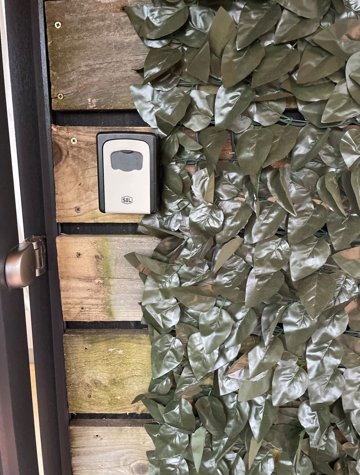 Une porte dotée d’un clavier de sécurité et d’un panneau en bois orné de motifs de feuillage vert.