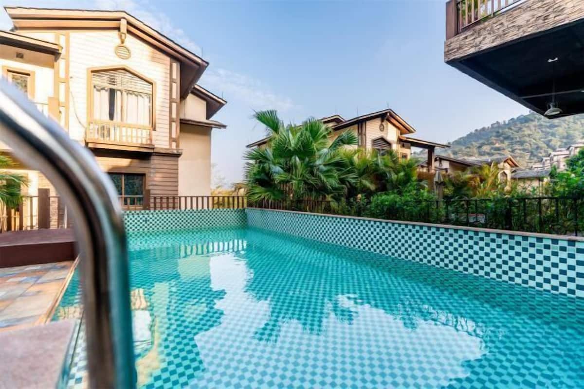 A swimming pool with a checkered pattern, surrounded by greenery and buildings.