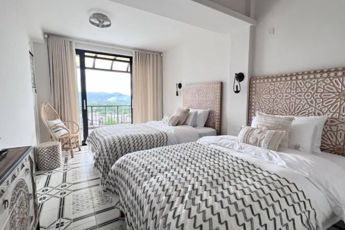 A hotel room with two beds, a balcony with a view, a patterned floor, and a decorative headboard.