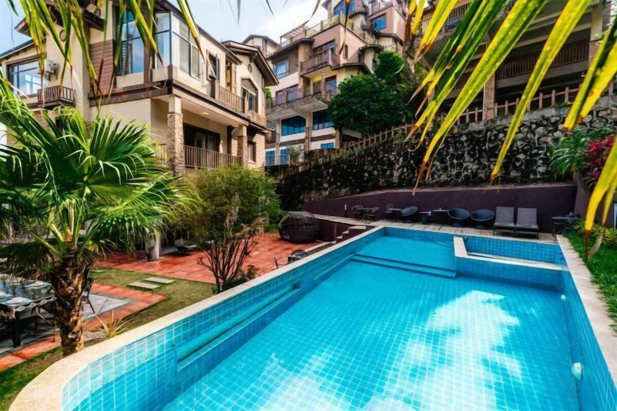 A swimming pool surrounded by a landscaped garden, with a multi-story building in the background.