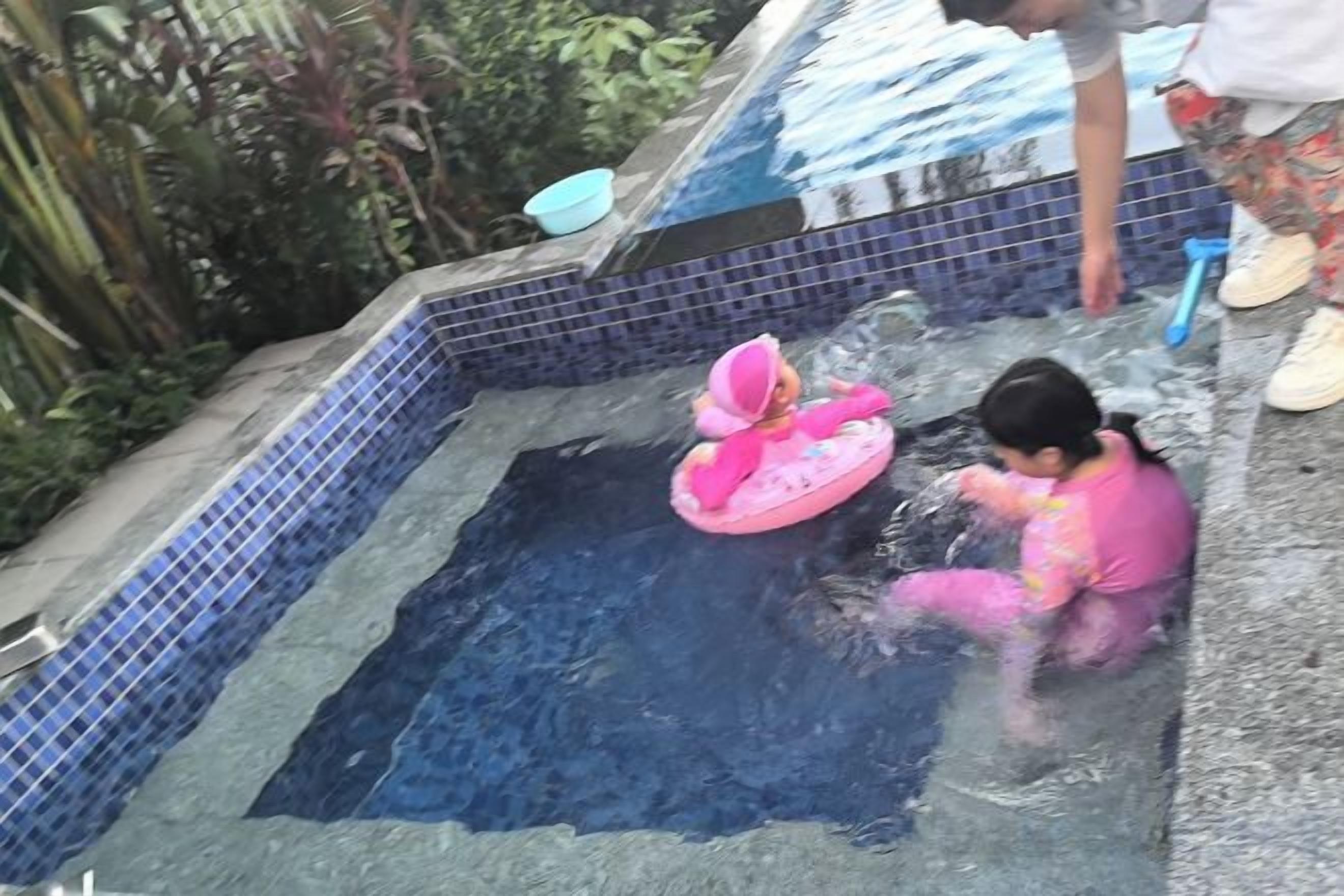 A child in a pink swimsuit playing in a small pool with a pink floatation device.