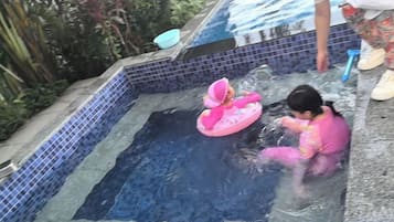 A child in a pink swimsuit playing in a small pool with a pink floatation device.