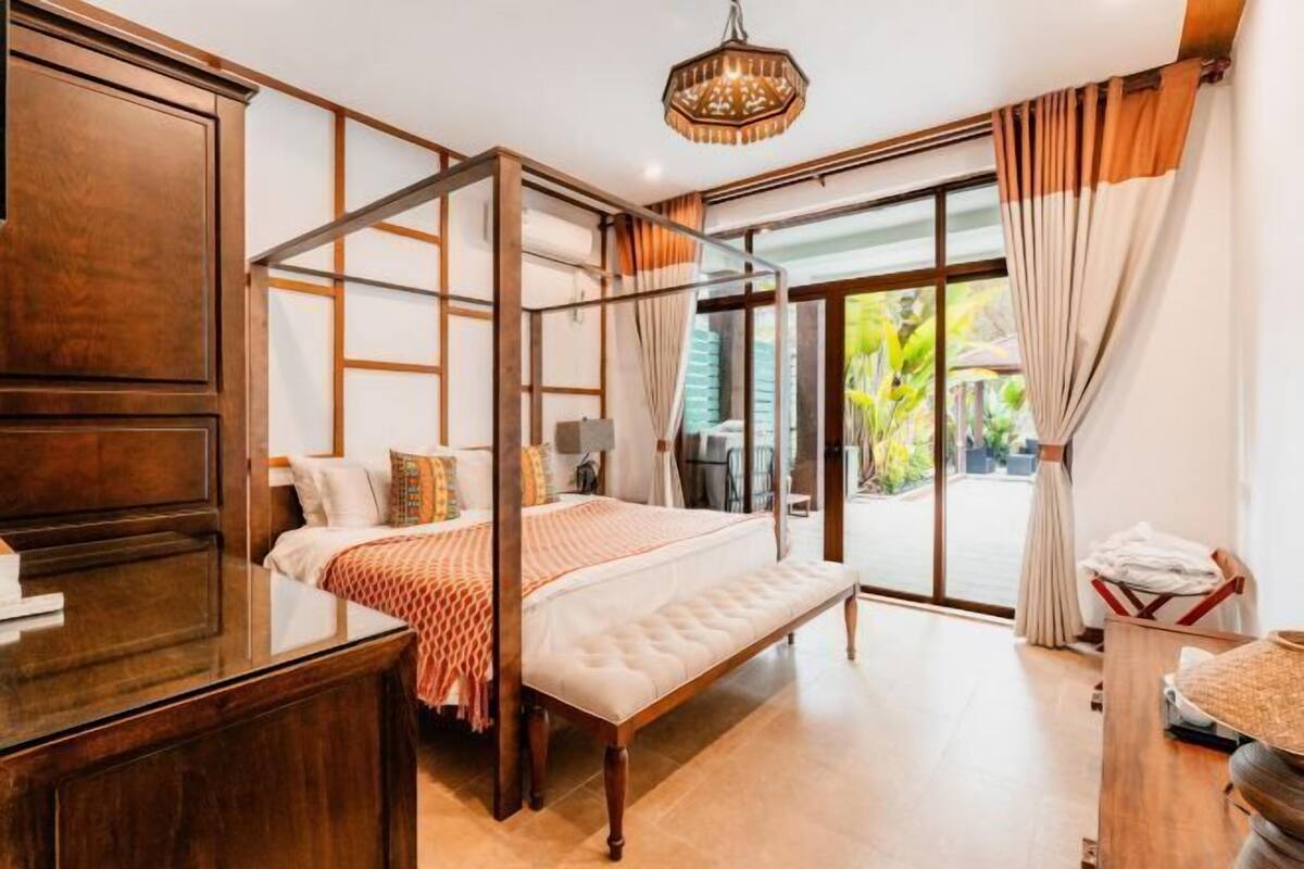 A bedroom with a four-poster bed, a wooden desk, and a view of the outdoors.