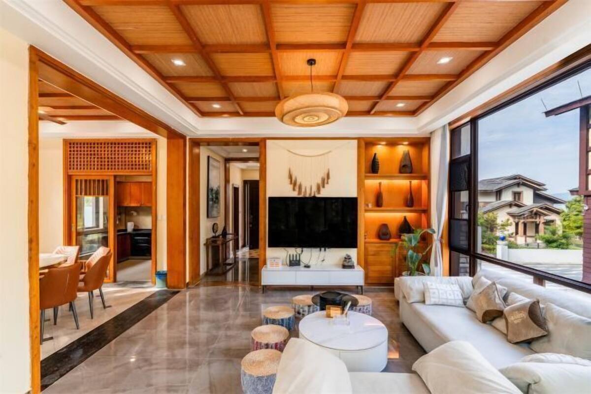 A modern living room with a wooden ceiling, a large TV, and a seating area with a sofa and round tables.