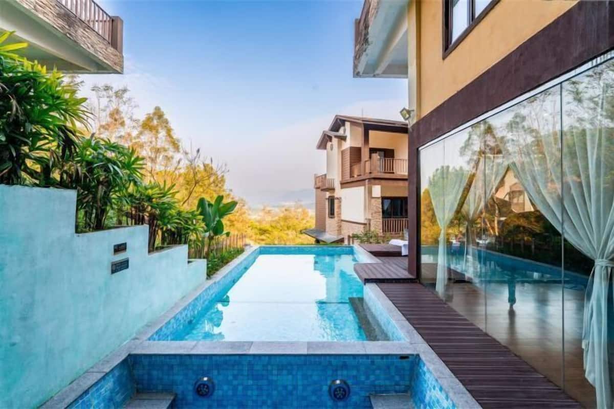 A swimming pool with a wooden deck, surrounded by plants and modern buildings.